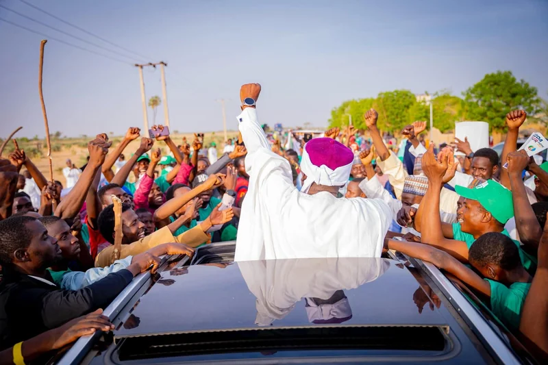 An outdoor gathering with people raising their hands around a vehicle